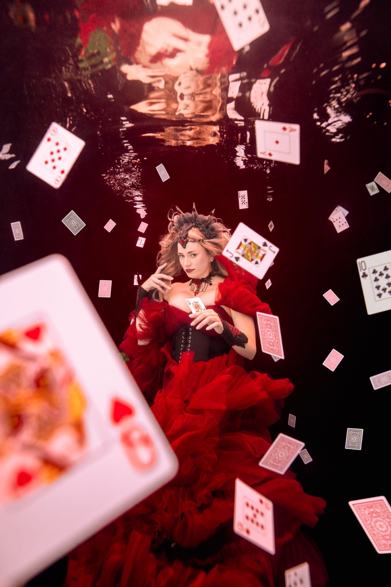 Underwater portrait of a model in a red gown surrounded by playing cards, by Kimber Greenwood, creative business mentor