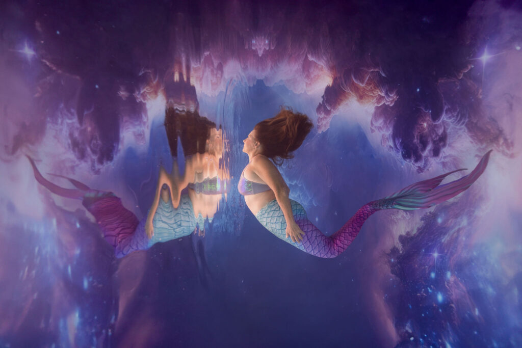 Mermaid posing underwater while reviewing technique with mentor