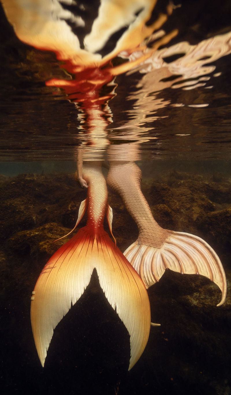 Mermaid in a golden tail resting on the sandy bottom of a Florida spring