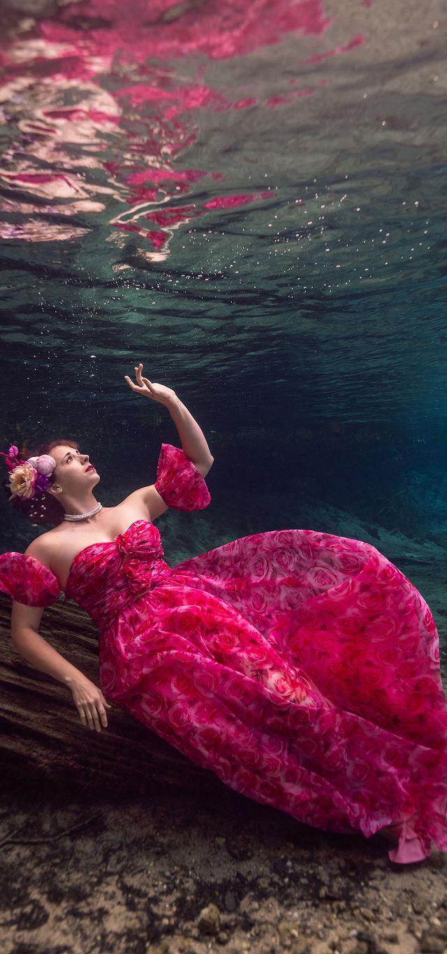 Expecting mother floating underwater in a flowing pink gown