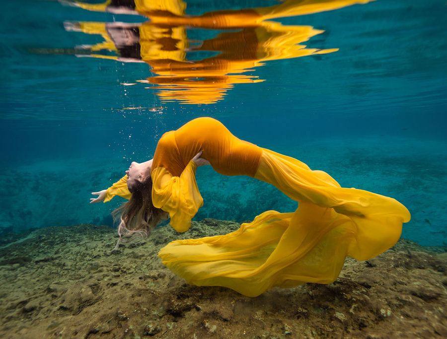 Expecting mother in a flowing gown photographed underwater in a pool