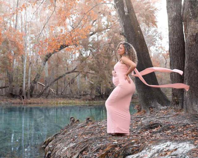 Pregnant woman in pink dress poses outdoors by a turquoise spring during a maternity photoshoot with Water Bear Photography