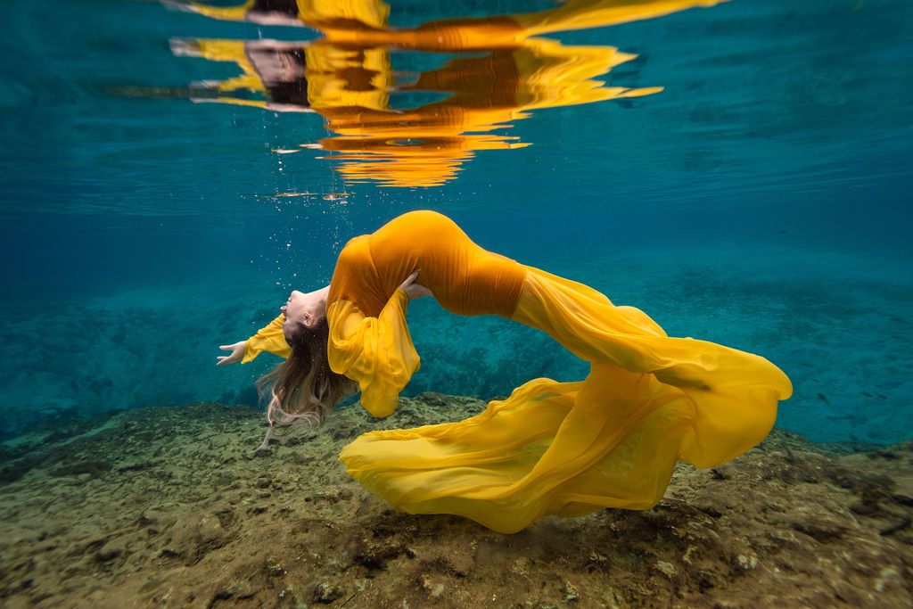 Expecting mother floating underwater in a flowing yellow gown