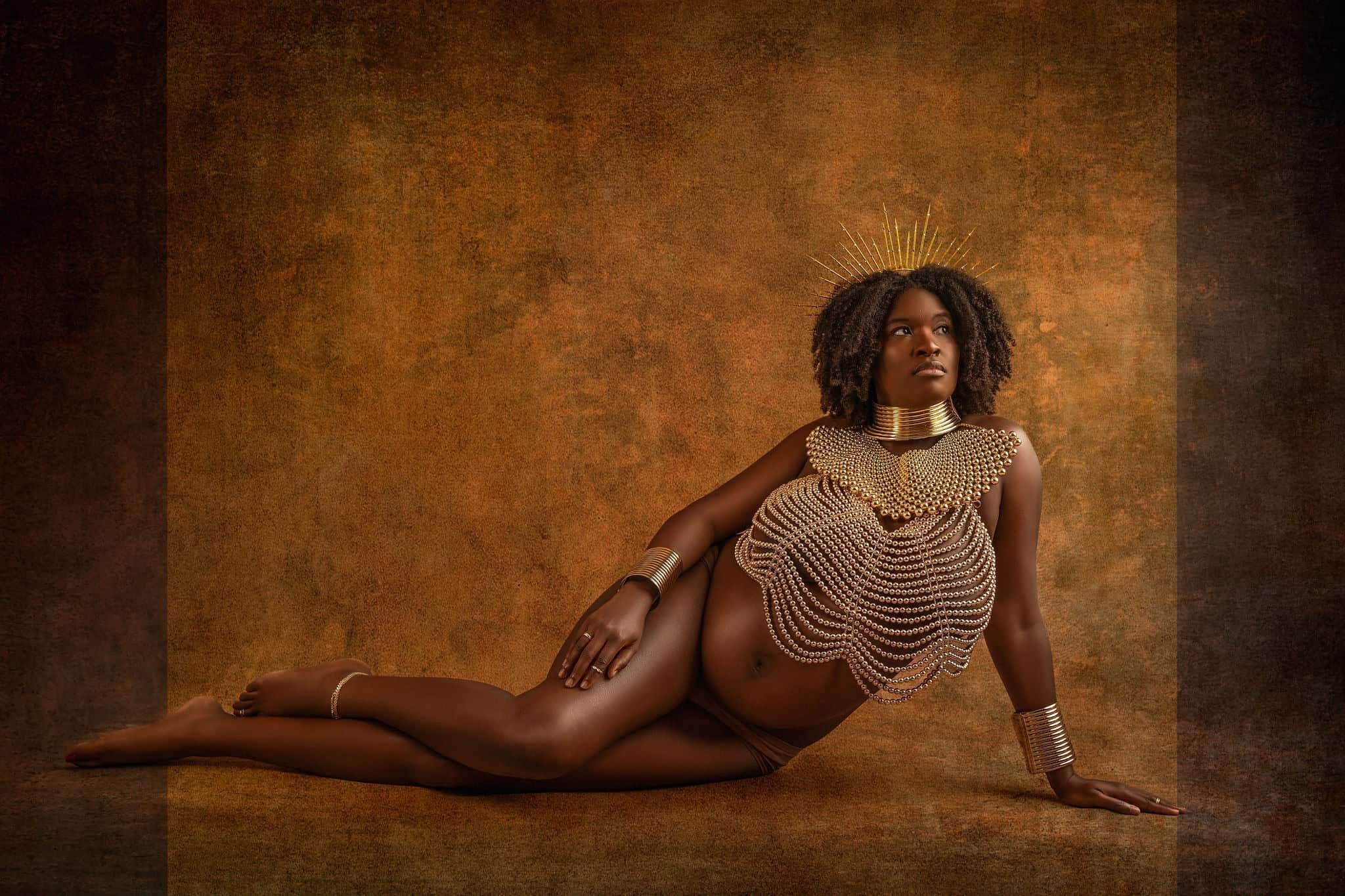 Pregnant black woman sits on floor during a studio maternity photoshoot with Water Bear Photography wearing African jewelry and a pearl body chain necklace
