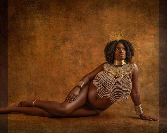Pregnant black woman sits on floor during a studio maternity photoshoot with Water Bear Photography wearing African jewelry and a pearl body chain necklace
