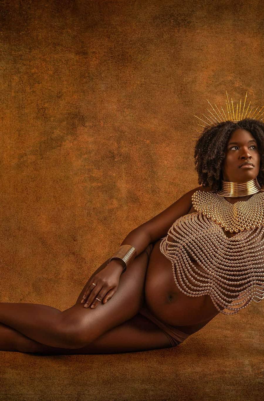 Pregnant black woman sits on floor during a studio maternity photoshoot with Water Bear Photography wearing African jewelry and a pearl body chain necklace