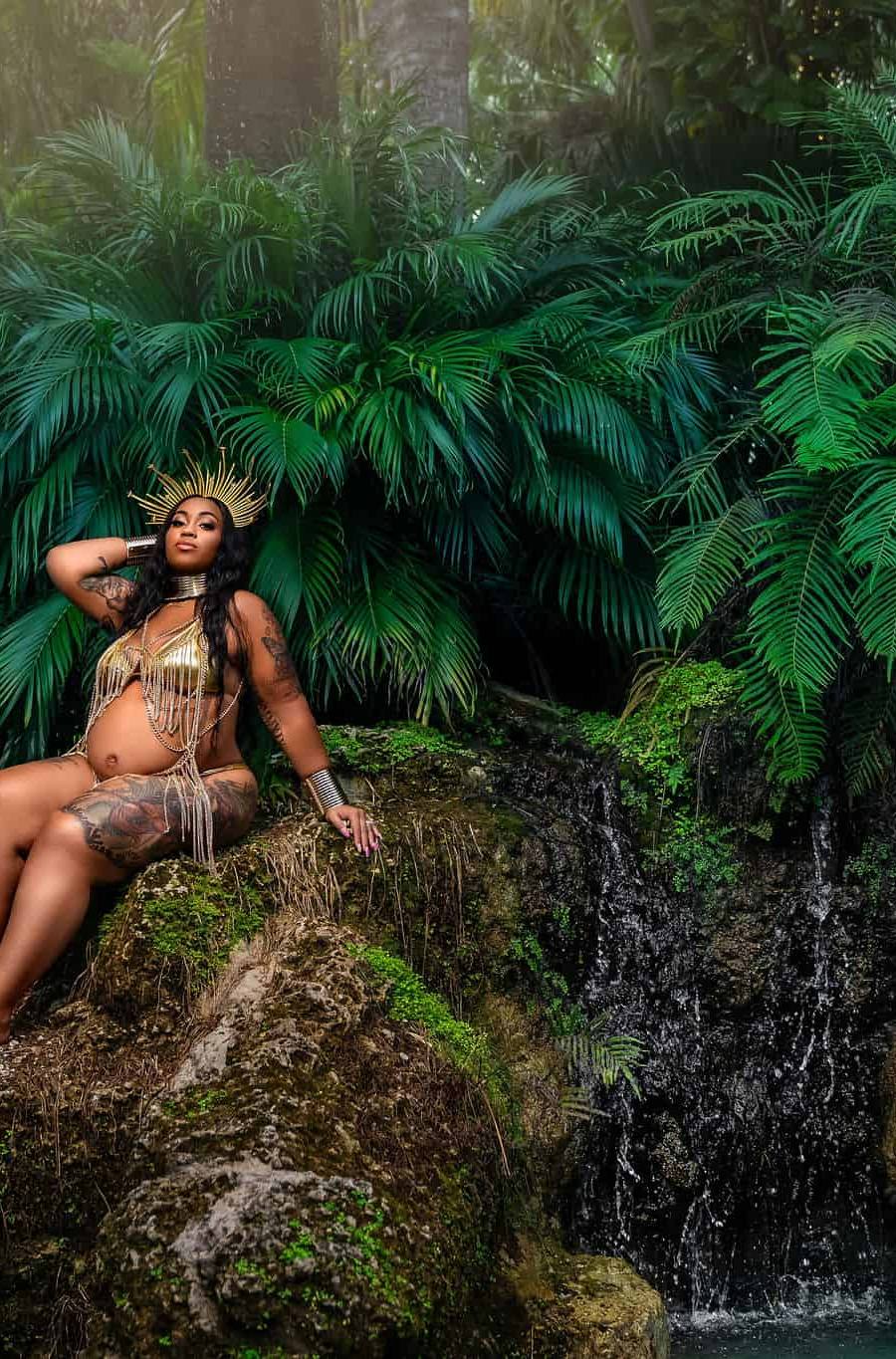 Pregnant woman sitting on moss covered rocks next to a waterfall at the Secret Gardens near Miami