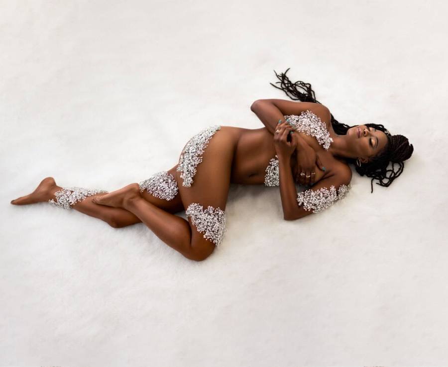 Black woman lays on a white rug covered in silver accents during a studio boudoir photoshoot