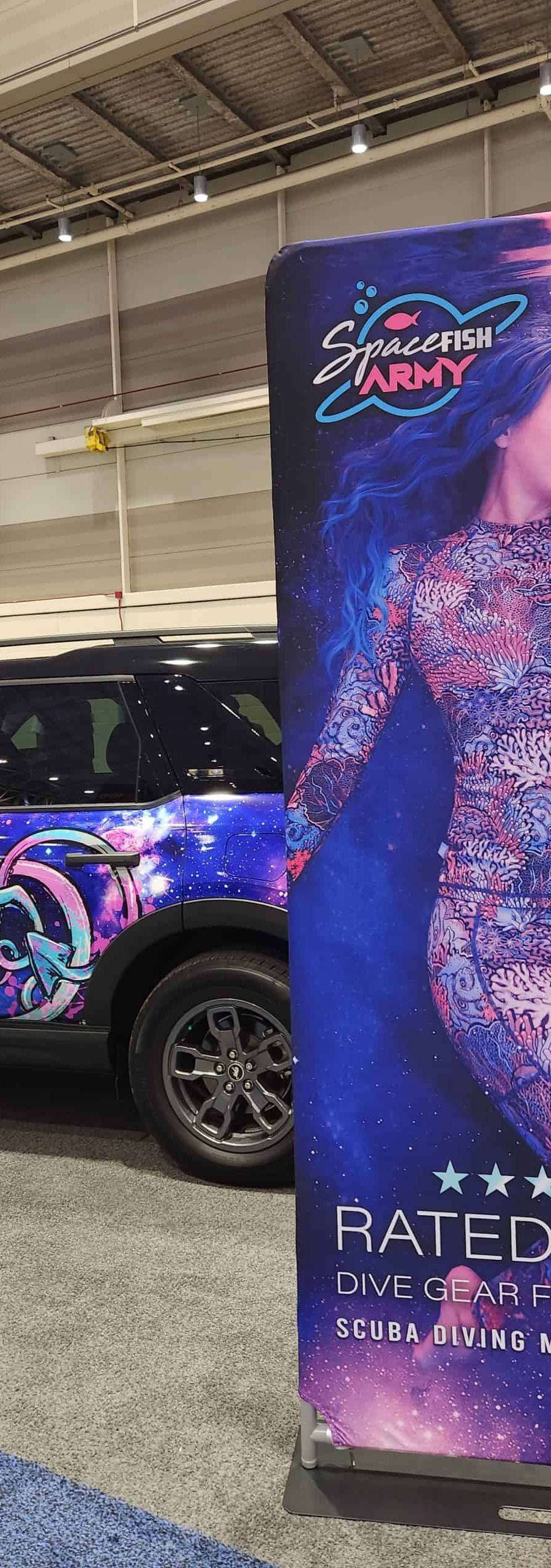 Banner on display at a scuba diving expo with a decorated truck in the background.