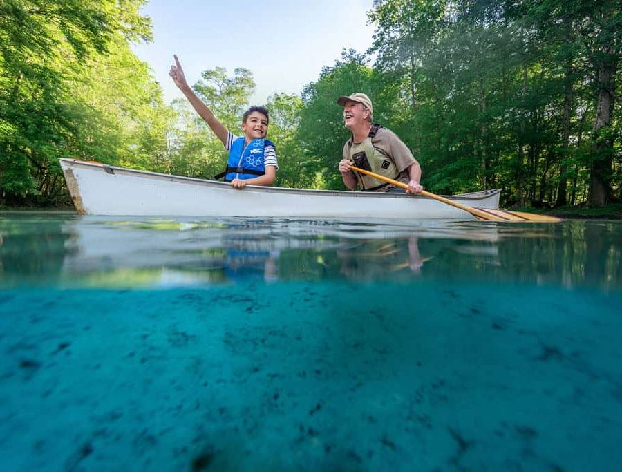A boy points towards a bird overhead while canoeing with his grandpa at a Florida spring.