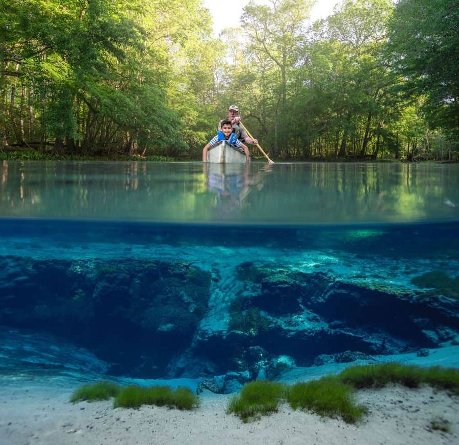 Boy and grandpa in a canoe floating over top of the basin of a Florida Spring.