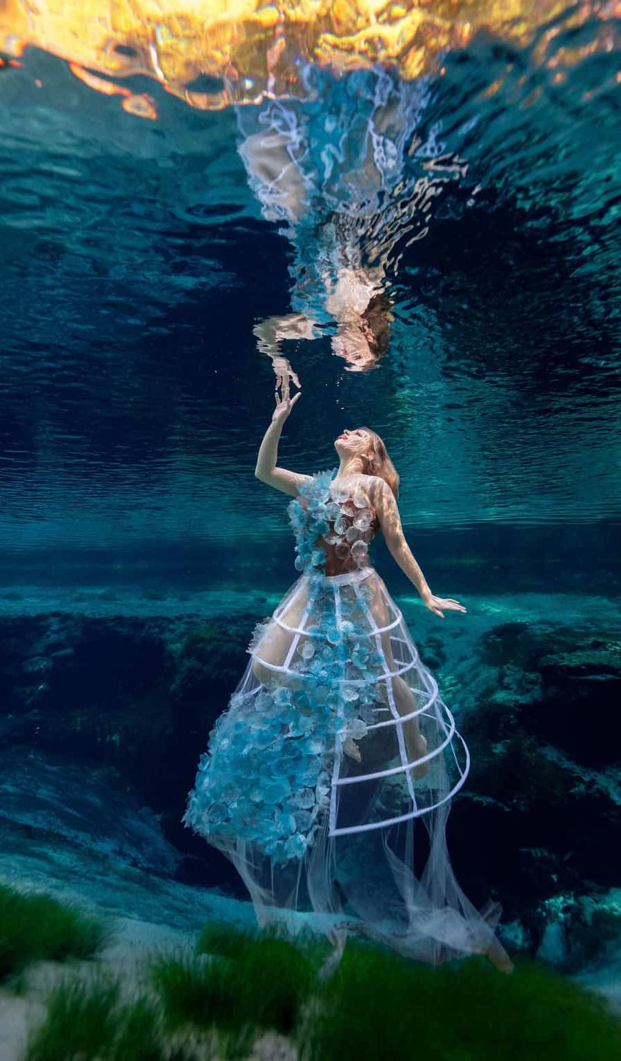 Woman floating in a Florida Spring wearing a dress made of plastic flowers, each one made from a locally bottled water bottle.