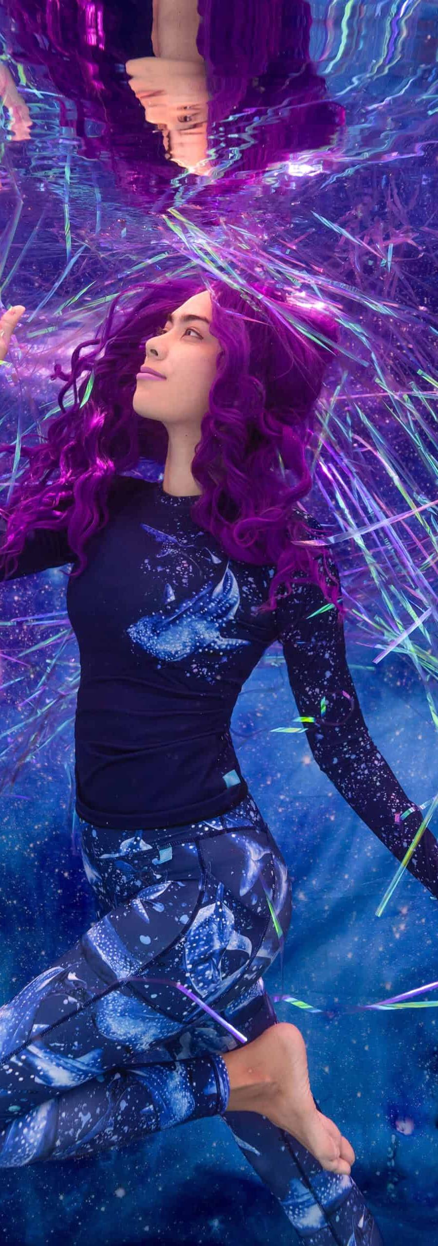 Model poses in Spacefish Army water sports apparel in a pool against a galaxy background and surrounded by shiny strings.