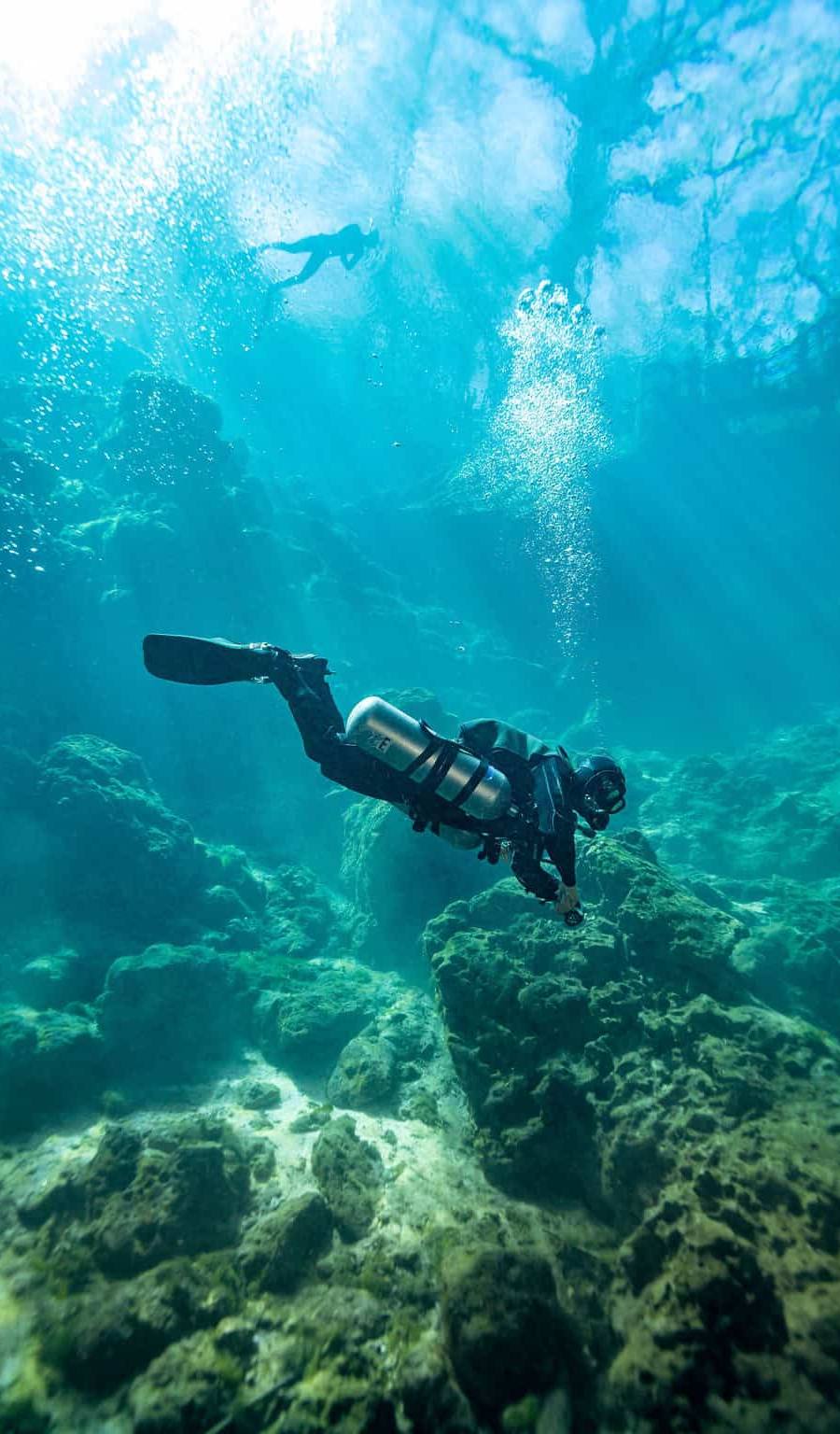 Scuba diver resting at the bottom of a Spring basin preparing to enter the underwater cave system.