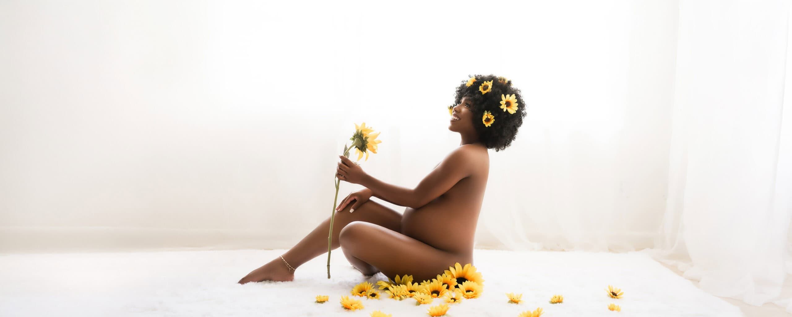 African American pregnant woman sits on a rug surrounded by sunflowers during a studio maternity photoshoot with Water Bear Photography in Gainesville, Florida