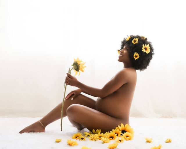 African American pregnant woman sits on a rug surrounded by sunflowers during a studio maternity photoshoot with Water Bear Photography in Gainesville, Florida