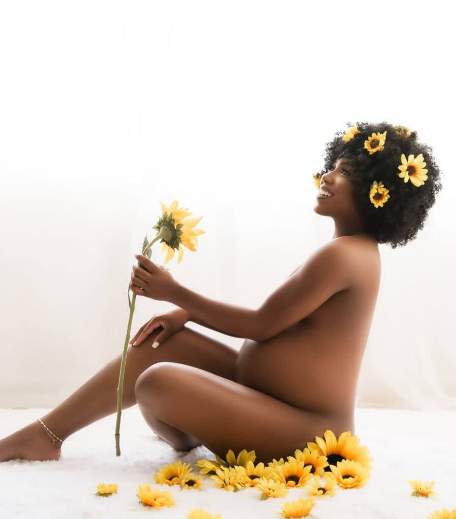 African American pregnant woman sits on a rug surrounded by sunflowers during a studio maternity photoshoot with Water Bear Photography in Gainesville, Florida