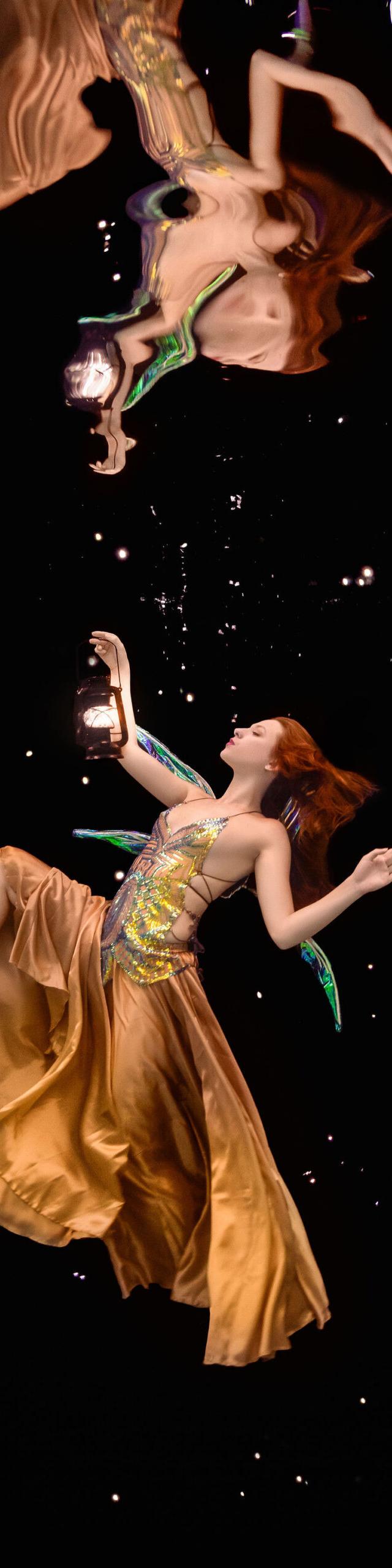 Model in an orange gown floating underwater surrounded by fish